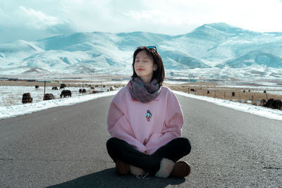 Young woman sitting on snow covered mountains against sky