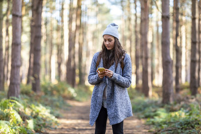 Woman standing by tree trunk in forest