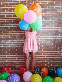 Woman holding colorful balloons against brick wall