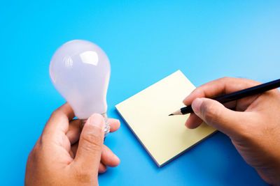 Close-up of hand holding paper against blue background