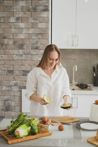 Smiling woman holding fruits standing in kitchen