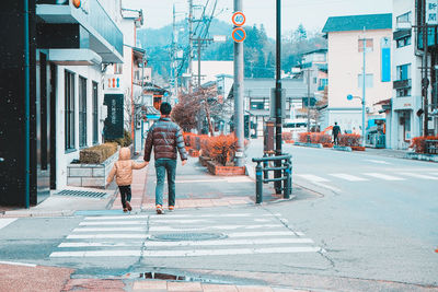 Rear view of people walking on sidewalk in city