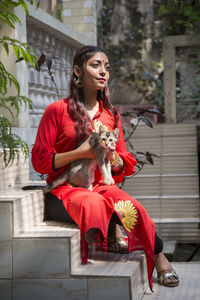 Young woman holding cat while sitting on steps