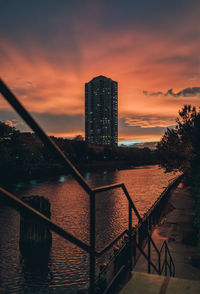 Buildings by river against sky at sunset