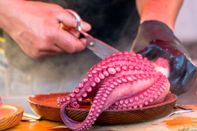 Midsection of vendor slicing octopus through scissor at fish market