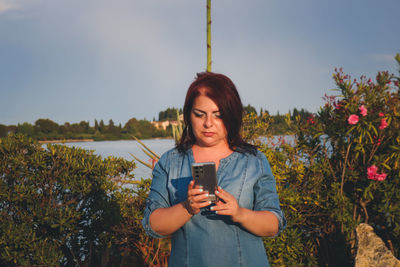 Young woman using mobile phone against plants
