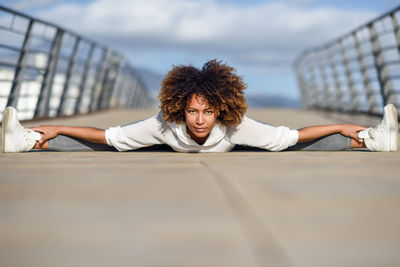 Portrait of smiling young woman with frizzy hair exercising on footbridge