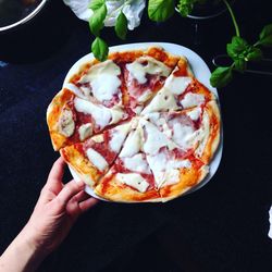 Cropped image of hand holding plate with pizza on table