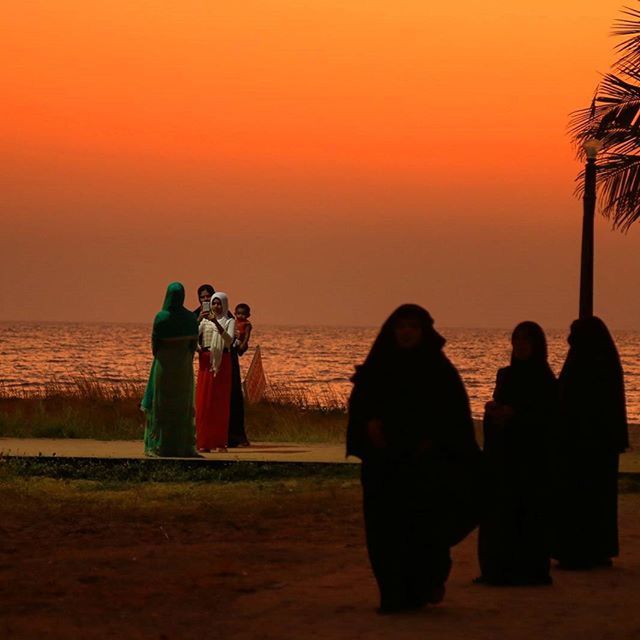 sunset, togetherness, sea, water, lifestyles, leisure activity, men, orange color, bonding, horizon over water, silhouette, clear sky, beach, person, rear view, love, standing, friendship