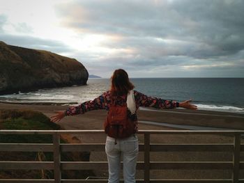 Rear view of woman standing at beach against sky