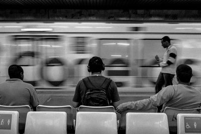 Rear view of men sitting against blurred motion of train at subway station