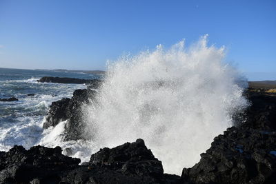 Waves splashing on rocks against clear sky