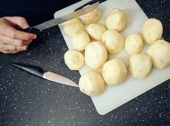 Cropped hand with knife by peeled potatoes on cutting board