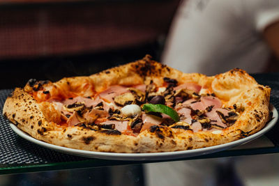 Traditional italian-style pizza with ham and mushrooms out of the oven on display.