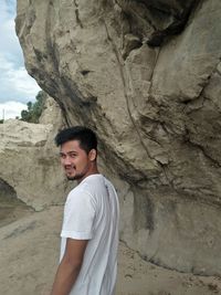 Side view portrait of young woman standing at beach by rock formation