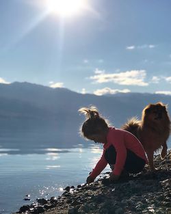 Girl crouching by dog against sea at beach