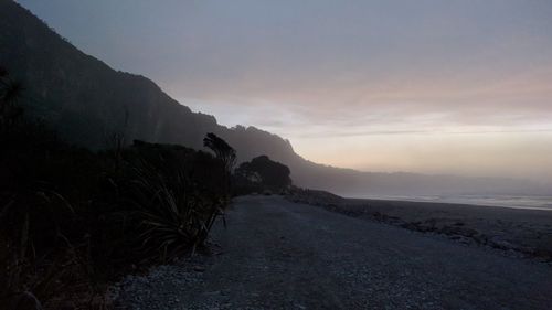 Road by sea against sky during sunset