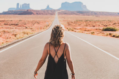 Rear view of woman standing on road amidst field