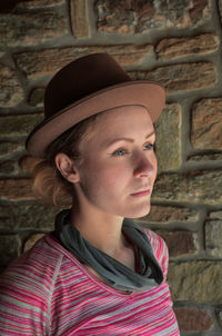 Close-up of woman in hat by brick wall