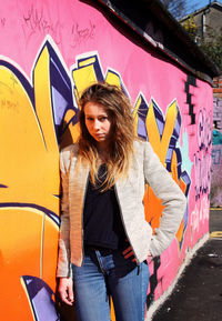 Rear view of young woman standing against graffiti wall