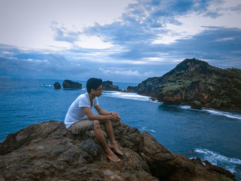 Woman sitting on rock by sea against sky