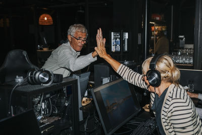 Male and female friends doing high five while playing computer game in gaming center