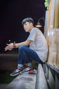 Side view of young man looking away while sitting against wall