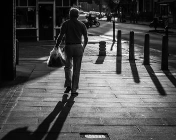 Rear view of woman walking with shopping bag on sidewalk in city