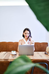 Female entrepreneur discussing business project on mobile phone while using netbook and working remotely at table in cafe