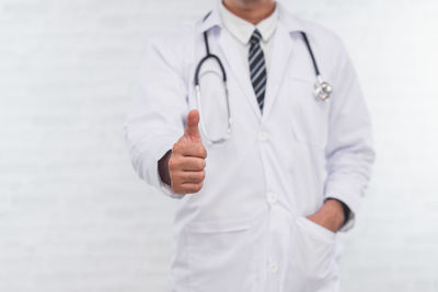 Midsection of doctor gesturing while standing against wall