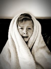 Portrait of scared boy wrapped in blanket on sofa