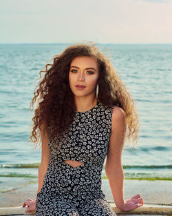 Portrait of young beautiful woman with curly hair against sea