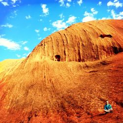 Low angle view of man sitting on mountain against sky