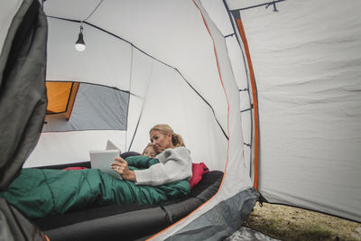 Mother and daughter using digital tablet while lying in tent at camping site