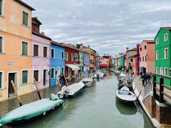 Boats moored in canal amidst buildings against sky with a lot of colors