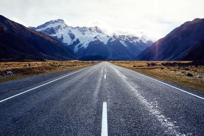 Empty road leading towards snowcapped mountain against sky