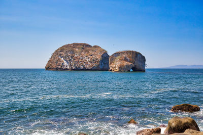 Rocks in sea against clear blue sky