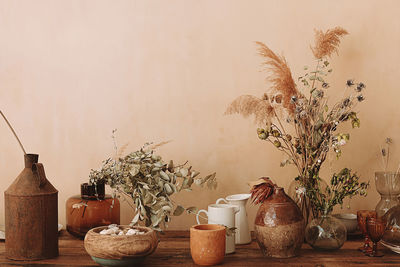 Lots of empty glassware and vases with dried flowers and plants on a wooden antique vintage table. 