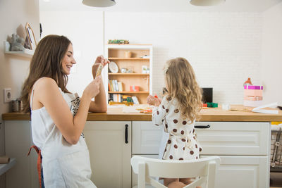 Mother photographing daughter preparing food on table at home