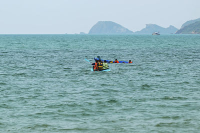 People kayaking in sea against clear sky
