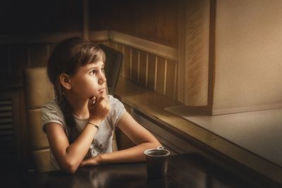 Girl looking away while sitting on table at home