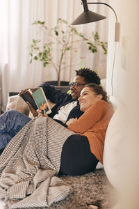 Man and woman reading books while sitting on sofa at home