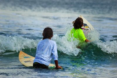 Rear view of girls surfing in sea