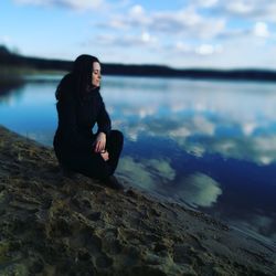 Woman sitting on rock at shore against sky