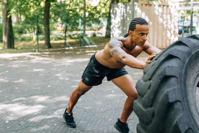 Full length of man lifting up tire on footpath