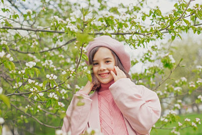 Portrait of a happy adorable little girl stands next to the branches of a blossoming apple tree
