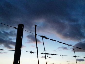 Low angle view of power lines against cloudy sky