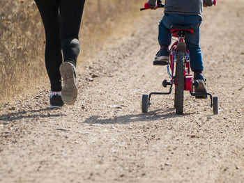 Low section of woman running by son cycling on road