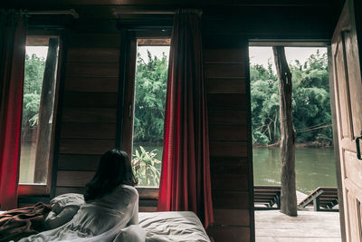 Rear view of woman sitting on window