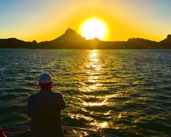 Rear view of silhouette man standing in sea against sunset sky